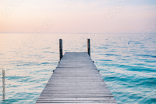 Wooden jetty pier on the sea at sunrise. Beautiful summer landscape in Italy