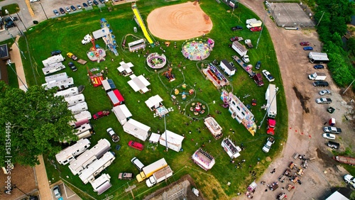 Bird's eye view of the amusement park on the green lawn surrounded by cars.