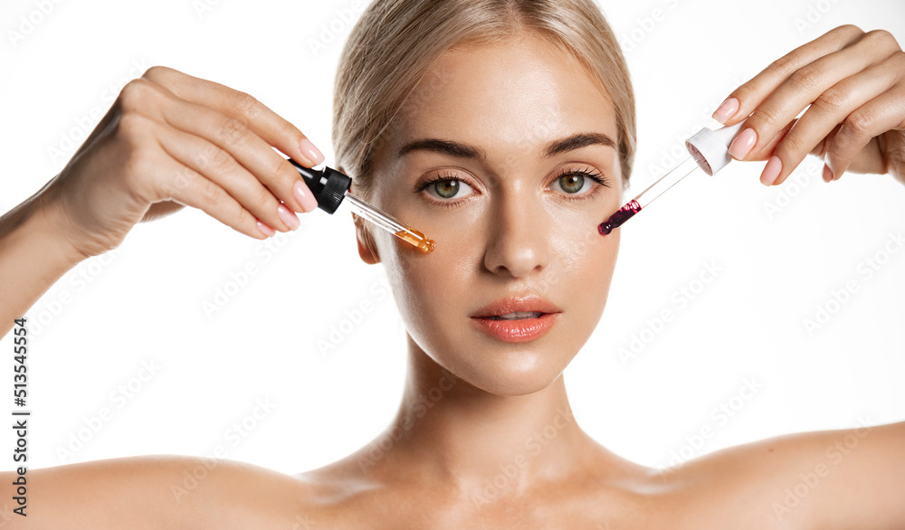Woman with two droppers of collagen, argan oil C-serum for beautiful young skin effect, using cosmetic products on her face, white background