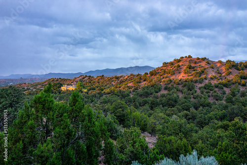 Sunset dusk in Santa Fe, New Mexico mountains in Tesuque community neighborhood with sunlight on houses, green plants and dark blue sky on high desert landscape