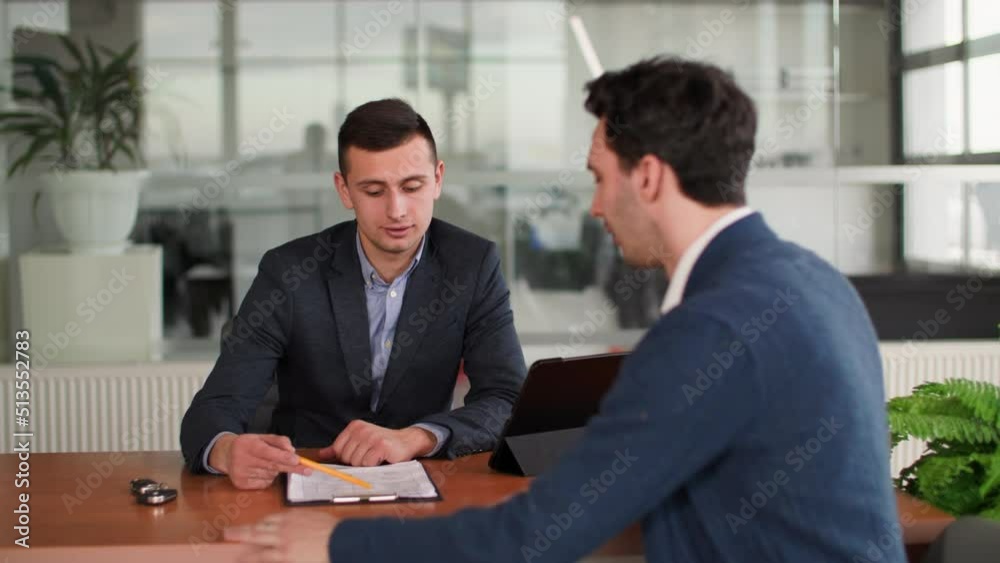 auto business, attractive car dealership manager talking to male buyer about choosing new automobile while sitting at table in vehicle center auto business, attractive car dealership manager talking to male buyer about choosing new automobile while sitting at table in vehicle center