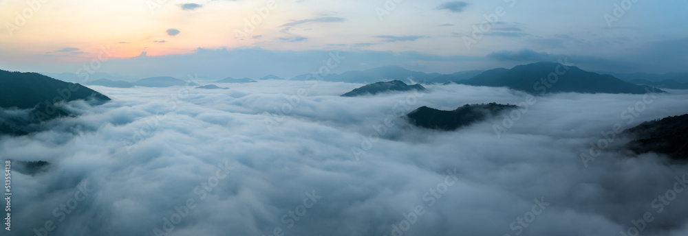 Panorama of sea of clouds around mountain peaks at sunrise