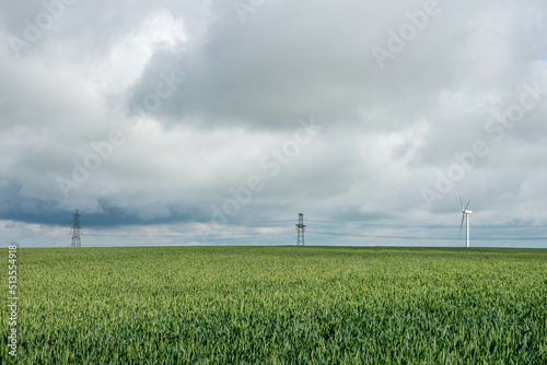 view from the Cotswold Way walk across a field of crops towards a wind turbine and pylons on a stormy summer day