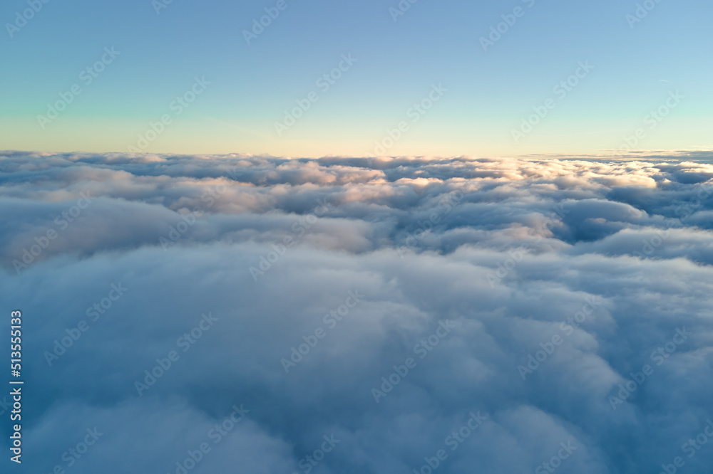 Aerial view from above at high altitude of dense puffy cumulus clouds flying in evening. Amazing sunset from airplane window point of view