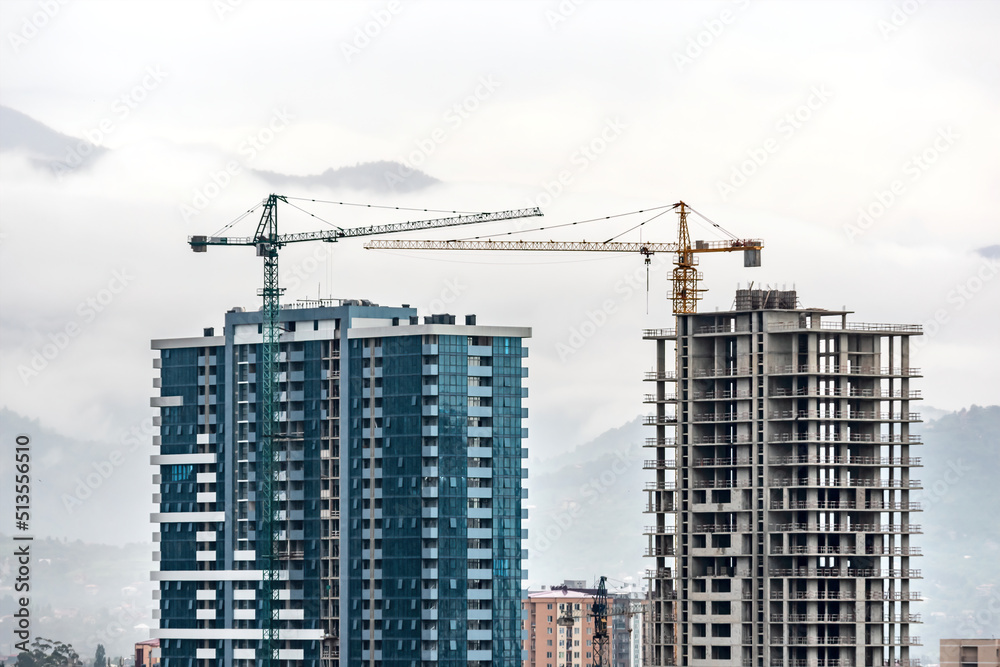 Construction site, cranes and multi-storey unfinished buildings over mist mountain background. Development building construction tall house apartment in skyscrapers Construction site, cranes and multi-storey unfinished buildings over mist mountain background. Development building construction tall house apartment in skyscrapers
