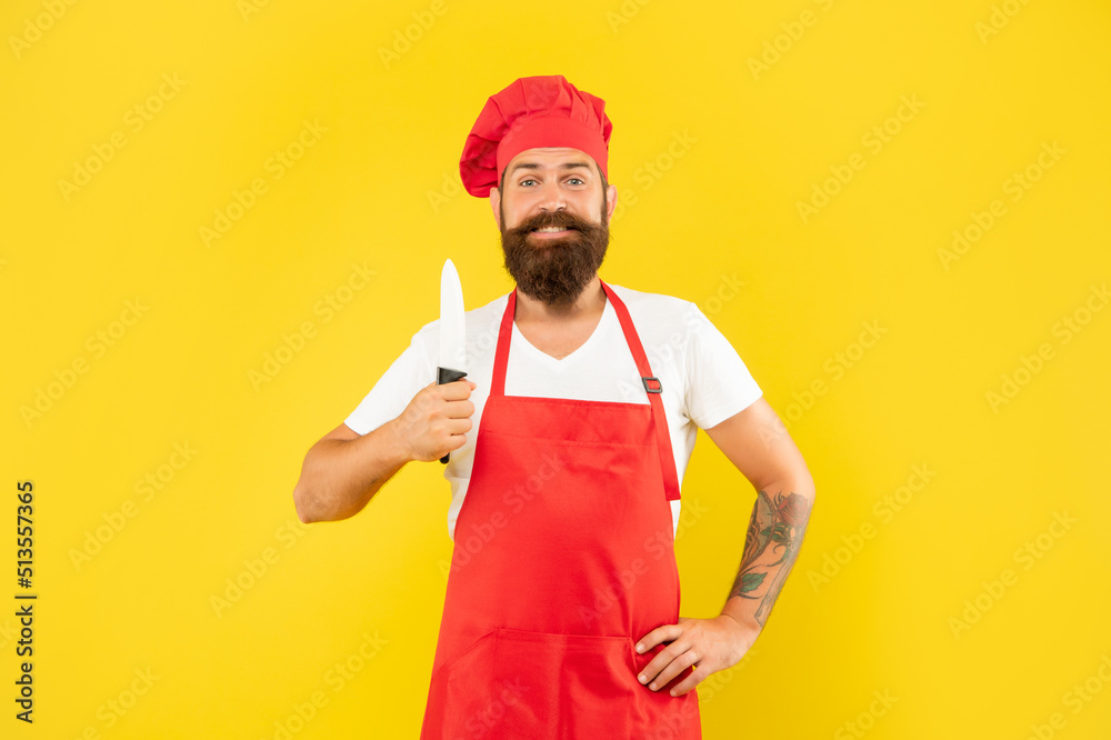 Happy man in red apron and toque holding cooks knife yellow background, cook Happy man in red apron and toque holding cooks knife yellow background, cook