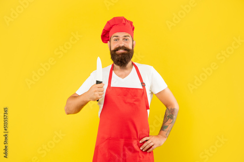 Happy man in red apron and toque holding cooks knife yellow background  cook