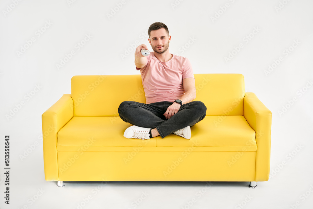 Young man watching TV with remote control sitting on comfort sofa