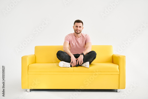Young trendy man posing sitting on yellow sofa looking to camera