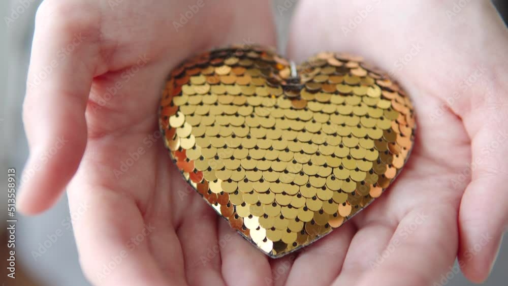 Golden shiny decorative shining heart in female hands.