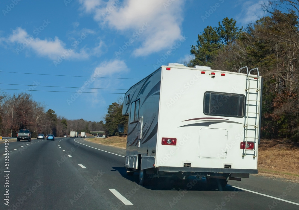 Rear view of recreation vehicle on highway with blue sky.
