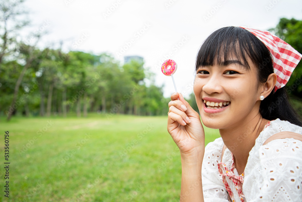 Asian beautiful woman holding Multi-Colored rainbow hard lollipop candy while picnic at the park. Concept of relaxing and special holiday Asian beautiful woman holding Multi-Colored rainbow hard lollipop candy while picnic at the park. Concept of relaxing and special holiday