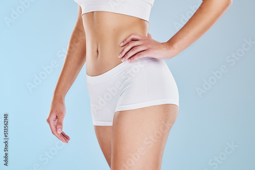Closeup of fit woman showing her stomach and body in underwear or sportswear, isolated against blue studio background with copyspace. Toned, sporty model standing alone. Slim physique and flat tummy