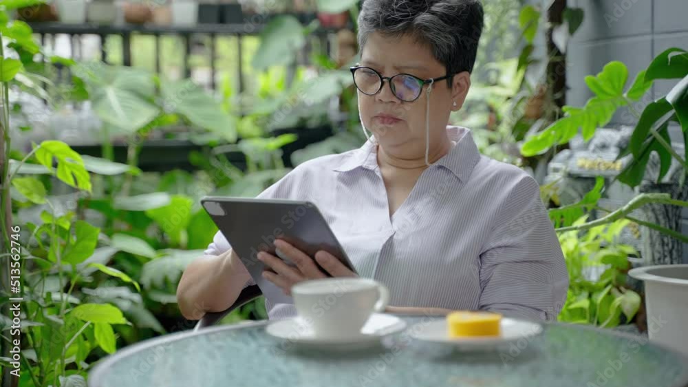 Asian elderly woman socializing through tablet in her home garden, concept of elderly people and technology. Asian elderly woman socializing through tablet in her home garden, concept of elderly people and technology.