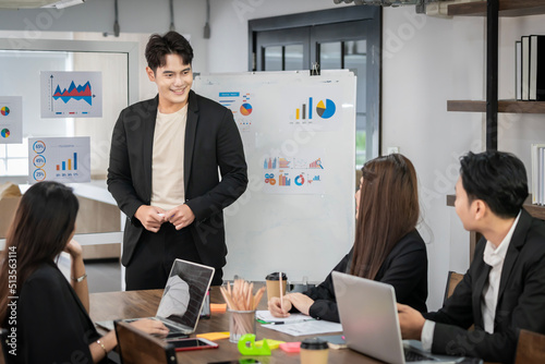 An Asian businessman is presenting his company performance report to his boss or group of male and female colleagues with confidence and professionalism.