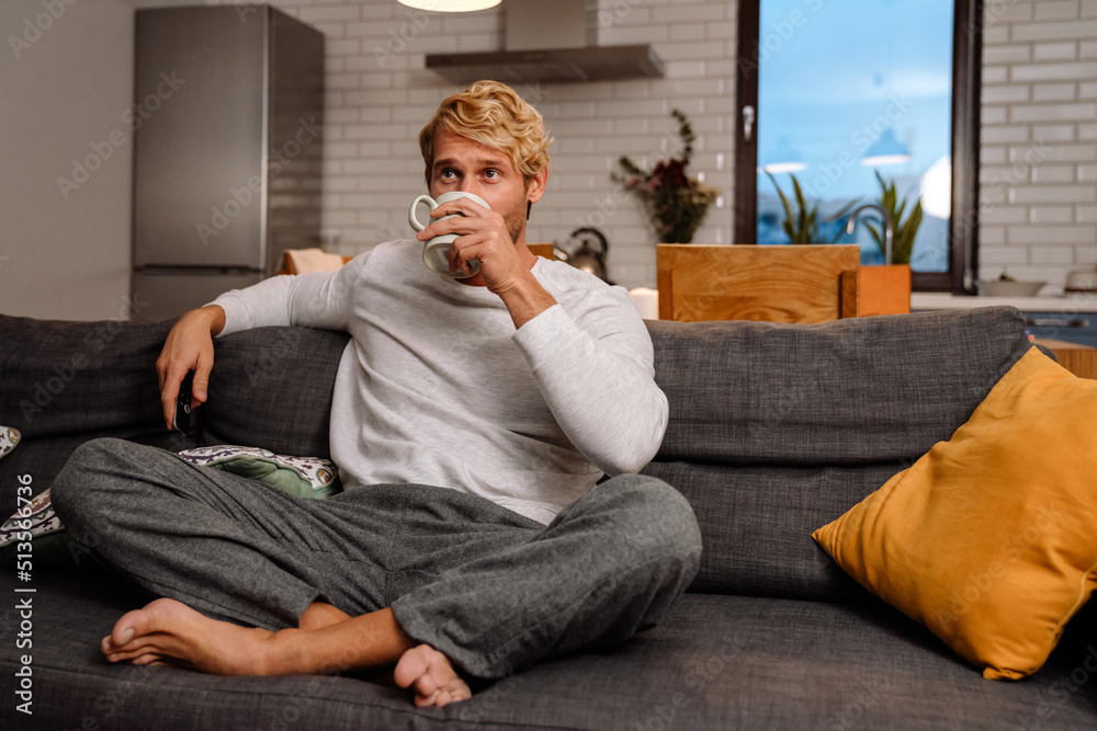 Blonde white man drinking tea while resting on sofa