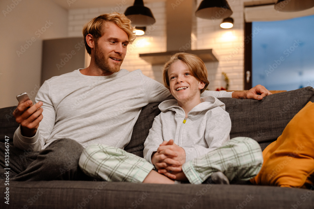 Ginger father and son smiling and watching tv while resting on couch Ginger father and son smiling and watching tv while resting on couch