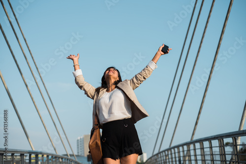 Working woman raises her hands in happiness and triumph on the street, holding a cell phone in her hand and is outdoors. Copy space