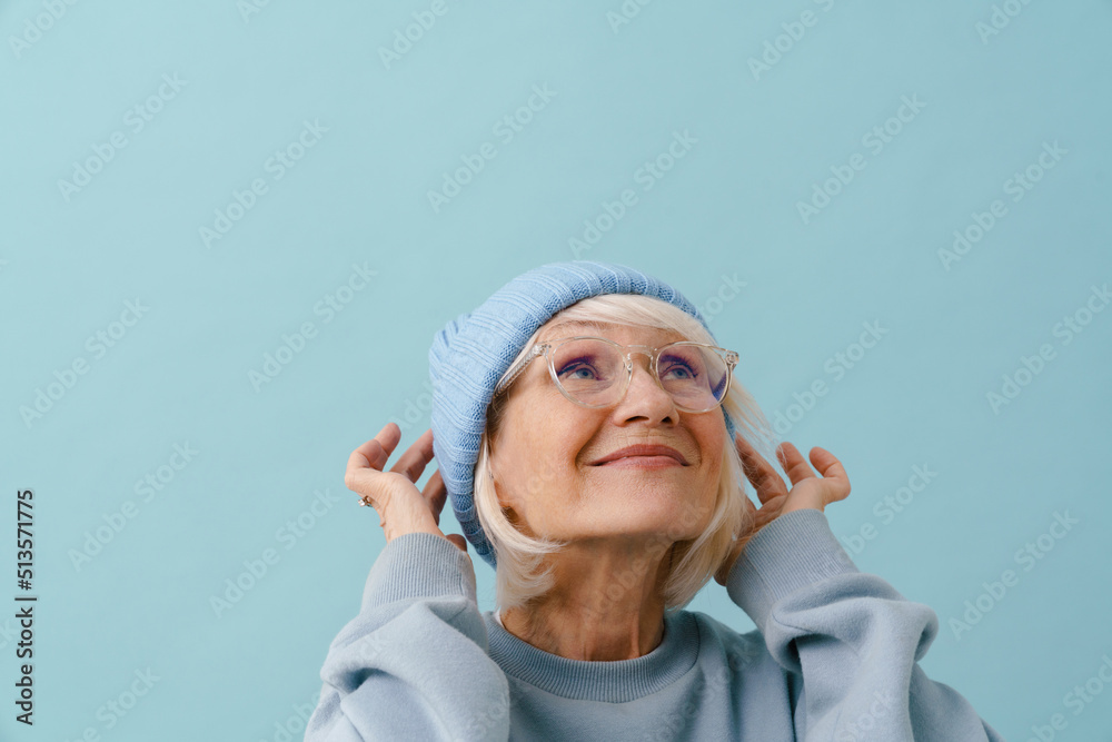 Beautiful smiling senior woman in glasses adjusting her winter hat