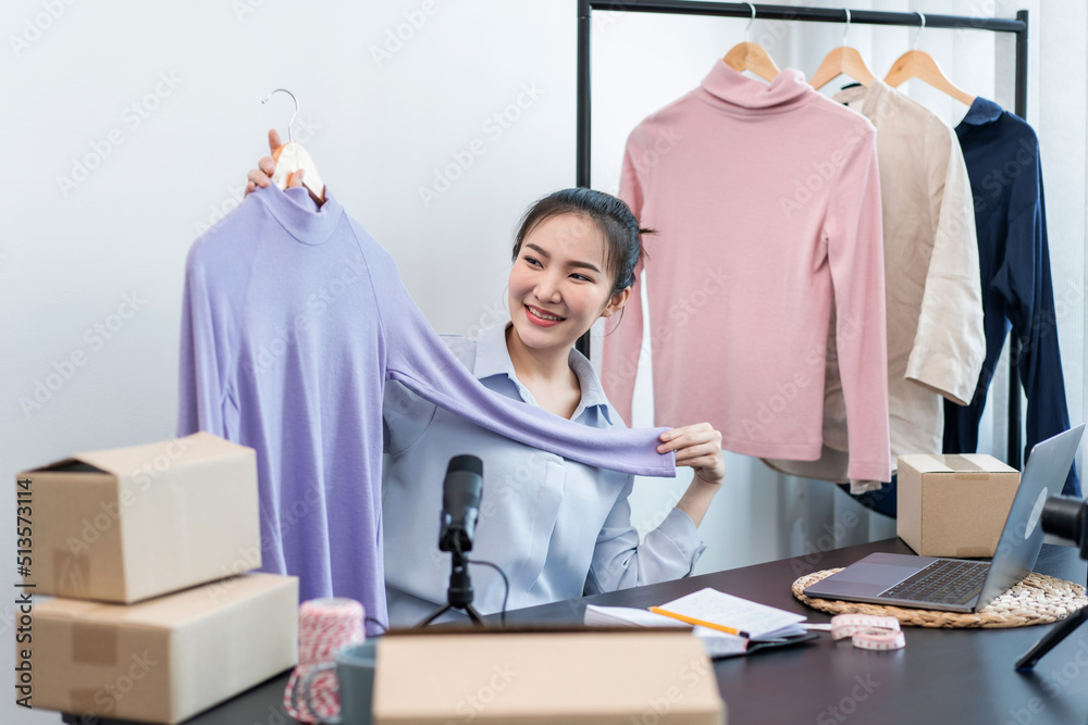 Fototapeta premium Women fashion designer stylist broadcast live streaming video to sale product and receive online order from customer and prepare packing clothes into boxes for sending delivery to client at home