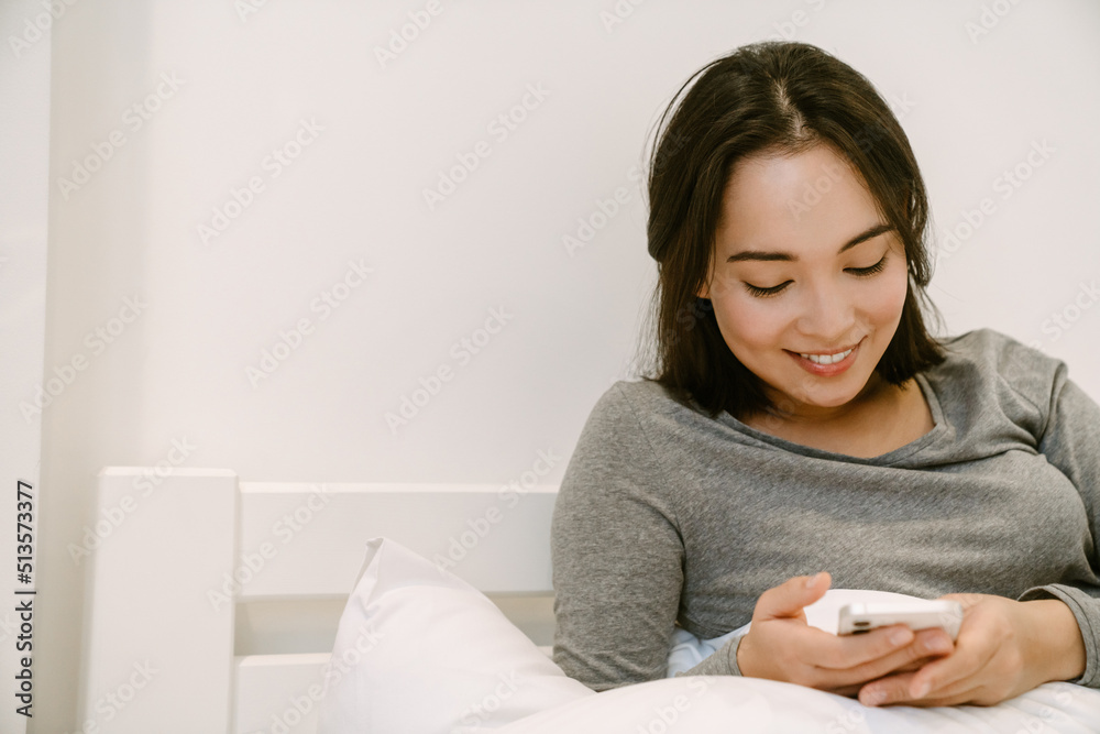 Young asian girl with phone sitting on the bed Young asian girl with phone sitting on the bed