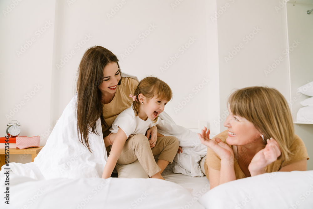 White girl playing with her mother and granddaughter in bed