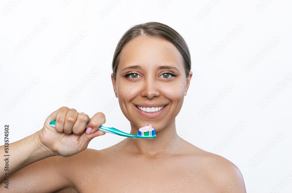 A young caucasian tanned smiling woman holding the toothbrush in her hand about to brush her teeth isolated on a white background. Morning and evening routine. Close up A young caucasian tanned smiling woman holding the toothbrush in her hand about to brush her teeth isolated on a white background. Morning and evening routine. Close up