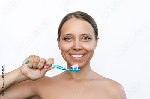 A young caucasian tanned smiling woman holding the toothbrush in her hand about to brush her teeth isolated on a white background. Morning and evening routine. Close up