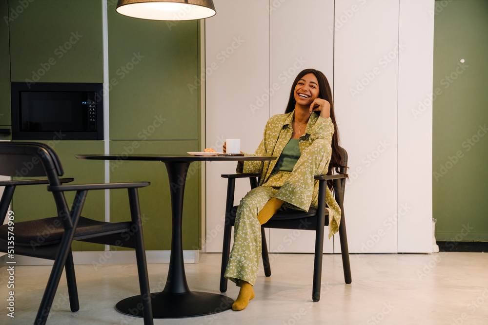 Young beautiful smiling long-haired woman sitting at kitchen table Young beautiful smiling long-haired woman sitting at kitchen table
