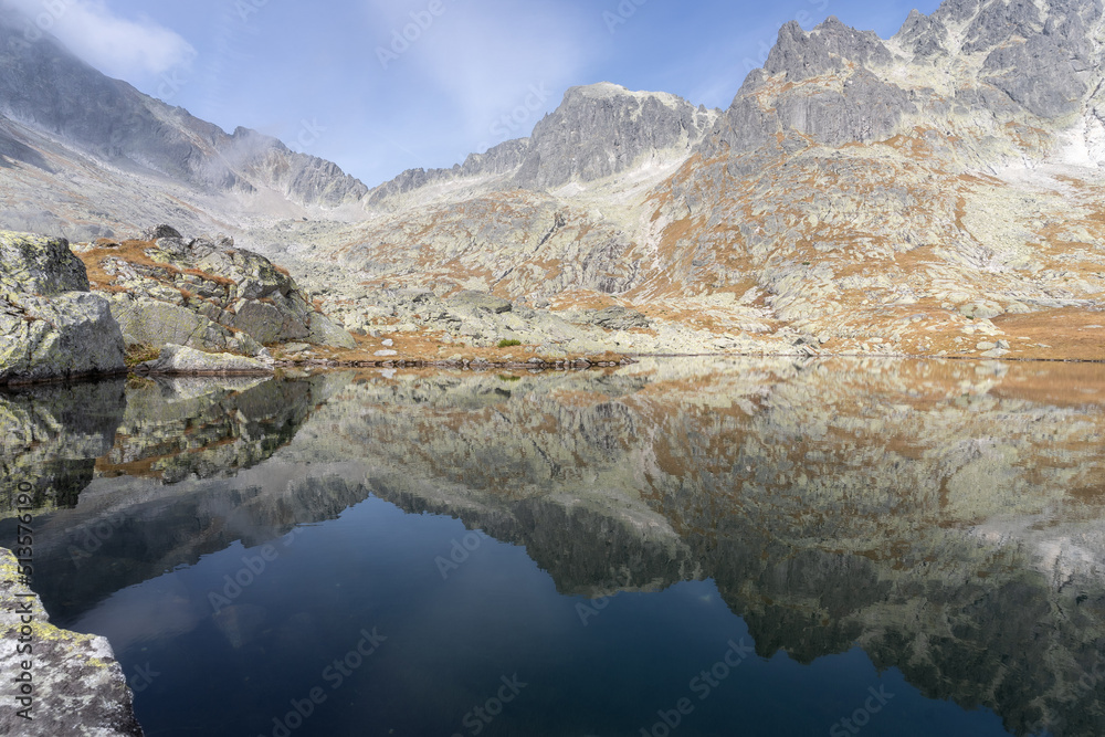 Still alpine lake reflecting rocky mountains with autumn colors surrounding it, Slovakia, Europe