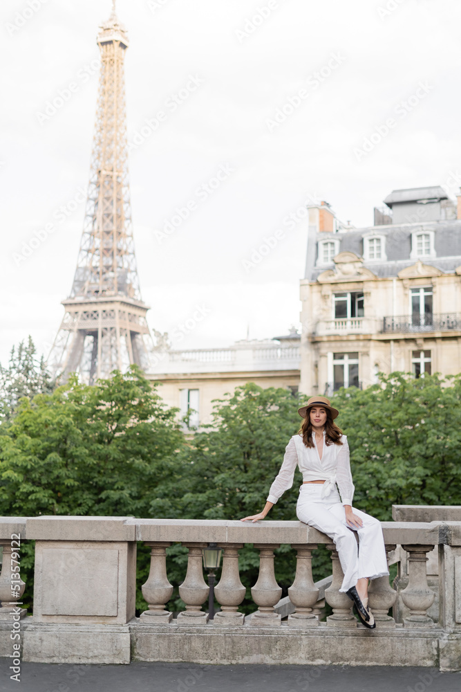 Fototapeta premium Fashionable woman holding smartphone and looking at camera on street with Eiffel tower at background in Paris.