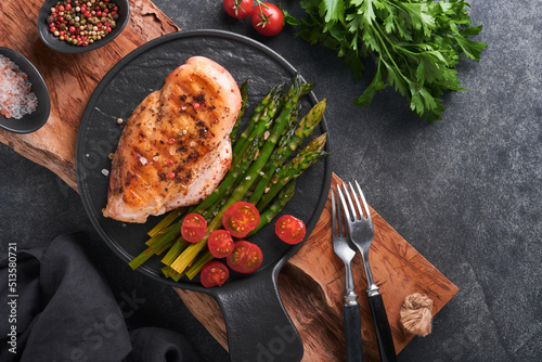 Chicken breast grilled with vegetables. Grilled chicken steak, asparagus and cherry tomatoes in black plate on gray concrete table background. Healthy diet lunch. Barbecue steak fried. Top view.