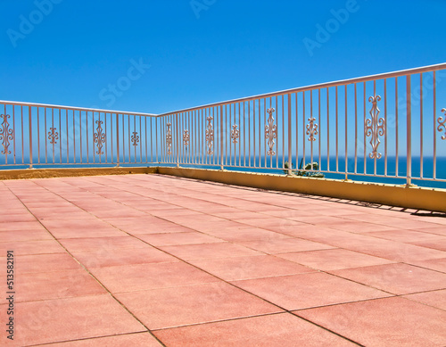 Beach house balcony or terrace with tiled floor and white fence. Summer view with a classic barricade overlooking the sea or ocean with a blue sky background. Seascape scenic view at a holiday lodge