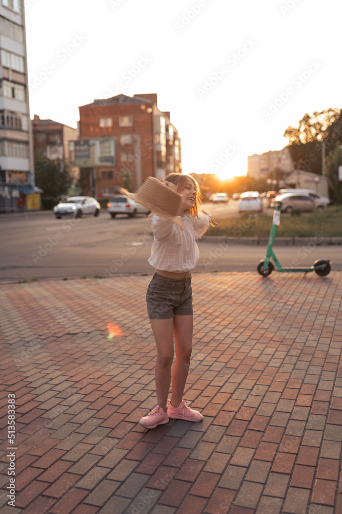 beautiful little girl in the city at sunset. A girl in a white blouse and with a straw hat is having fun outside