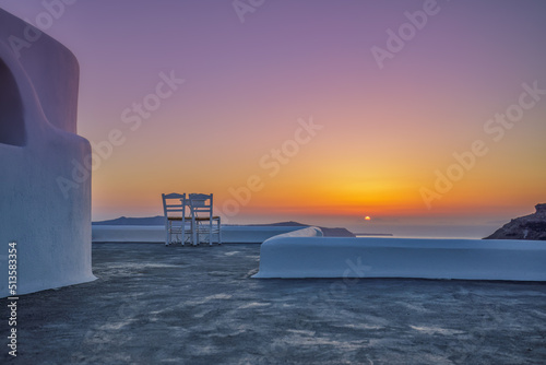 White architecture in romantic sunset light on Santorini island, Greece. Couple chairs on caldera terrace with sea view, beautiful colorful skyline sky view. Honeymoon panoramic travel background 
