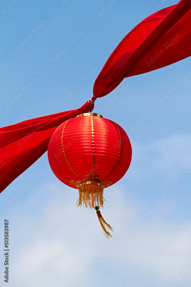 Obraz premium Red Chinese lantern in the air decorating the streets of China. Traditional Asian decor for new year celebrations in beautiful sky background. Creative cultural art hanging high up on a summer day