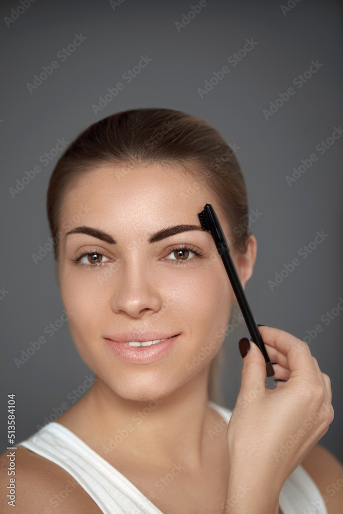 Beauty model. Correcting and contouring eyebrows. Beautiful woman shaping brows with comb.