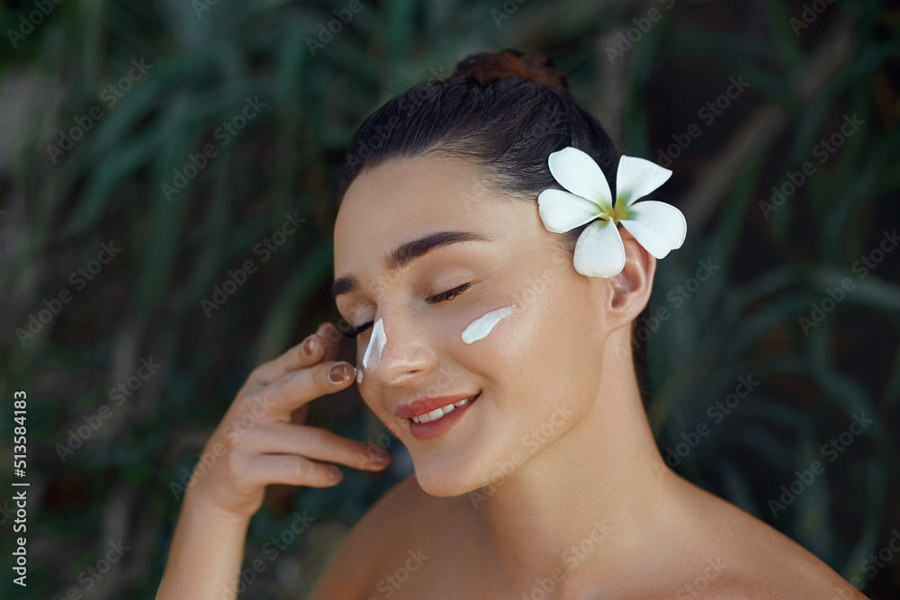 Beauty Woman Concept. Skin care. Young model with Soft skin holding cosmetic cream. Portrait of female applying moisturizing cream and touch own face in tropical nature Beauty Woman Concept. Skin care. Young model with Soft skin holding cosmetic cream. Portrait of female applying moisturizing cream and touch own face in tropical nature
