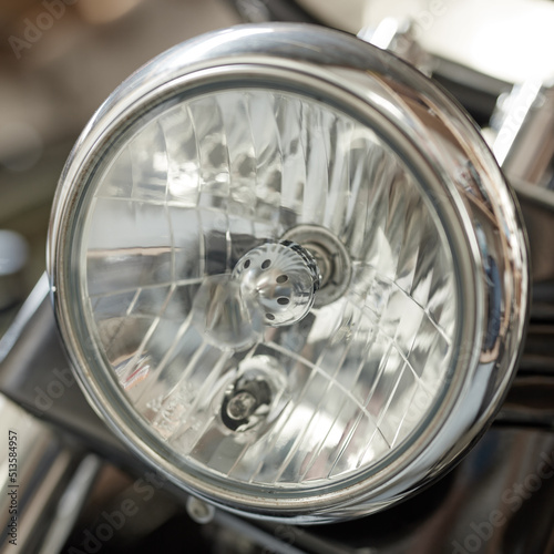 Closeup of a round headlight on a classic motorbike. One light bulb on a well maintained sliver chrome coated retro motorcycle. Motor vehicle accessories and parts. Glass lamp light with silver fram © Dhoxax/peopleimages.com