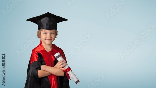 Cute kid wearing graduation cap and ceremony robe with certificate diploma. Graduate celebrating graduation. Education Concept. Successful elementary school