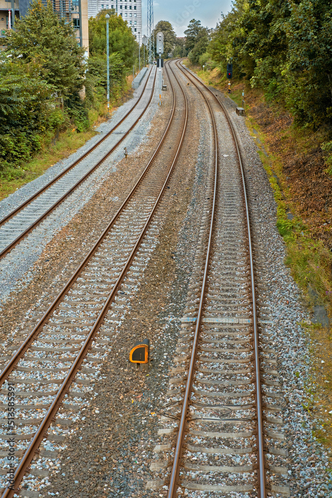 Fototapeta premium View of three old railway tracks leading out of a city in Denmark. Travel and commute by public train to work. Abandoned steels rails for freight trains, transportation, import and export industry
