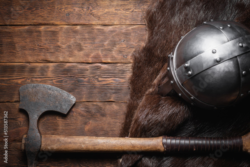 Viking axe, helmet and beast skin on the wooden table flat lay background with copy space. photo