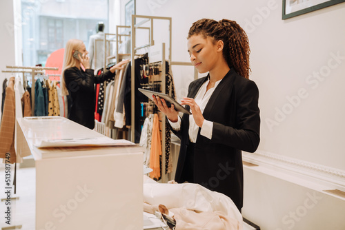 Happy saleswomen in uniform smiling while working in clothes store photo