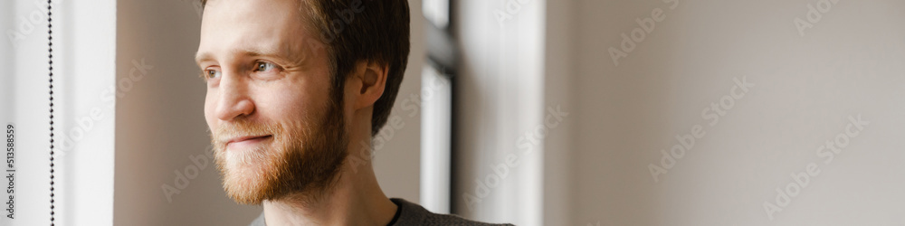 Obraz premium Ginger young man using mobile phone while leaning on wall indoors