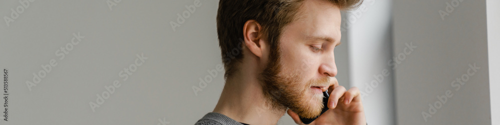 Obraz premium Ginger young man talking on mobile phone while standing indoors