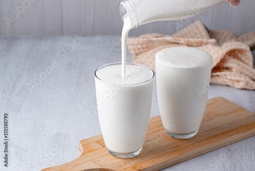 Pouring homemade kefir, buttermilk or yogurt with probiotics. Yogurt flowing from glass bottle on light background. Probiotic cold fermented dairy drink. Trendy food and drink. Copy space.