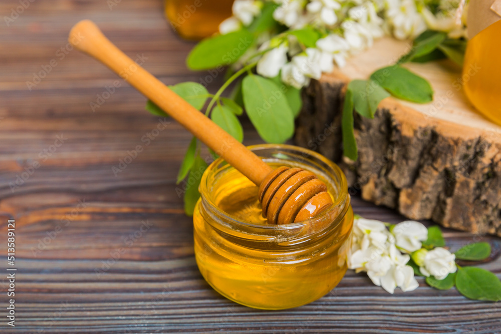 Sweet honey jar surrounded spring acacia blossoms. Honey flows from a spoon in a jar. jars of clear fresh acacia honey on wooden background Sweet honey jar surrounded spring acacia blossoms. Honey flows from a spoon in a jar. jars of clear fresh acacia honey on wooden background