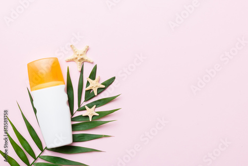 Sunscreen spray bottle. Bottle with sun protection cream and sea shells with tropical green leaf on color background, top view