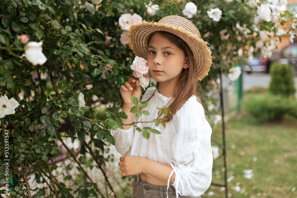 portrait of a beautiful girl with long hair and freckles in a straw hat outside in the summer near roses