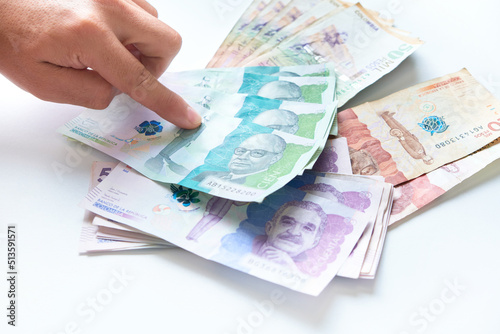 hand of a man pointing to a pile of various Colombian peso bills on a white table.